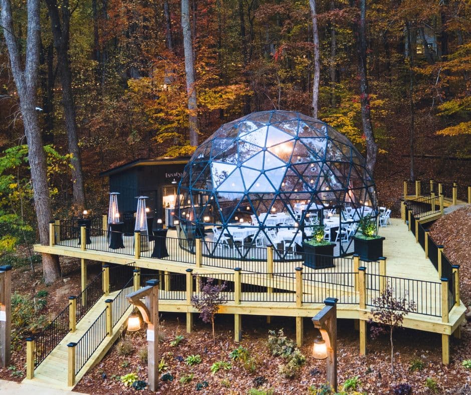 EkoDome glass dome lit at dusk in autumn woods